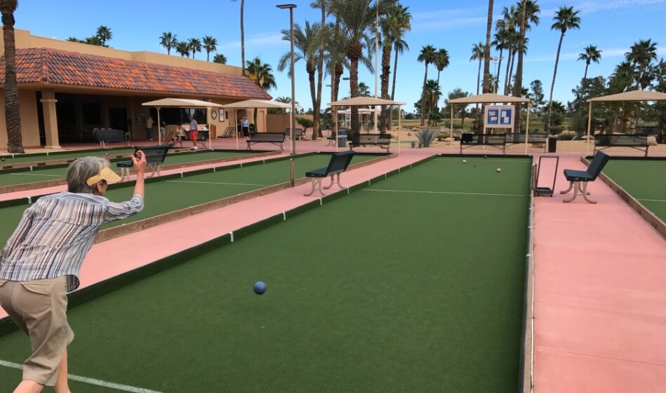 an older person in an active pose lunging to roll a bocce ball down the court