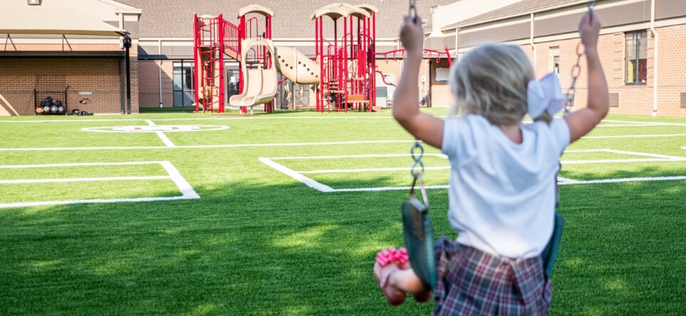 a little girl on a swingset at a school playground surfaced with XGrass synthetic turf