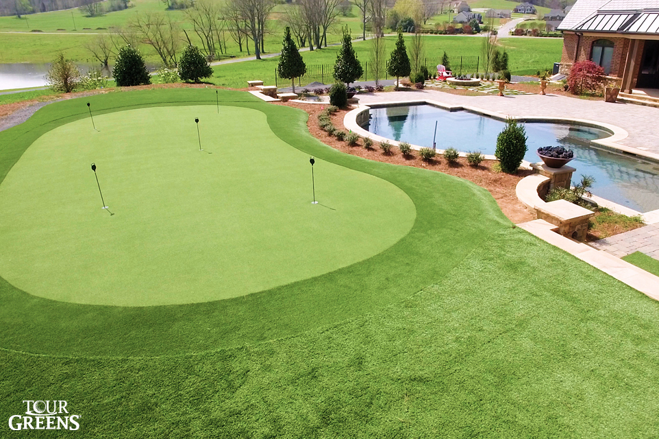 Large backyard installed with a large putting green area by a swimming pool